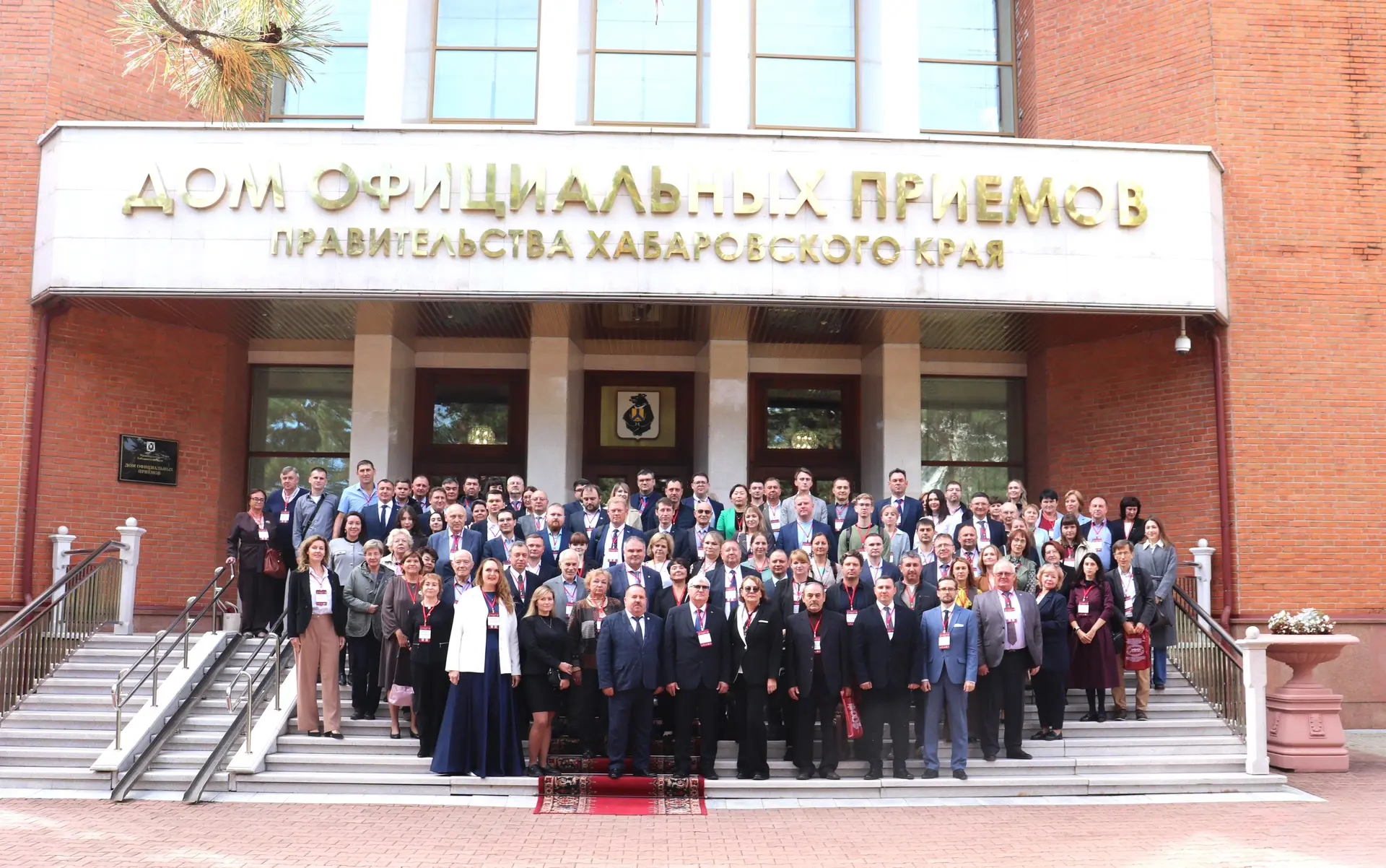 A group of people stands on a staircase in front of a building with the inscription 'House of Official Receptions of the Government of Khabarovsk Krai'.