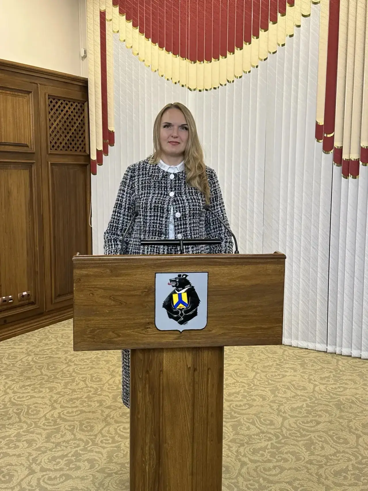 Женщина в деловой одежде выступает за трибуной в помещении.