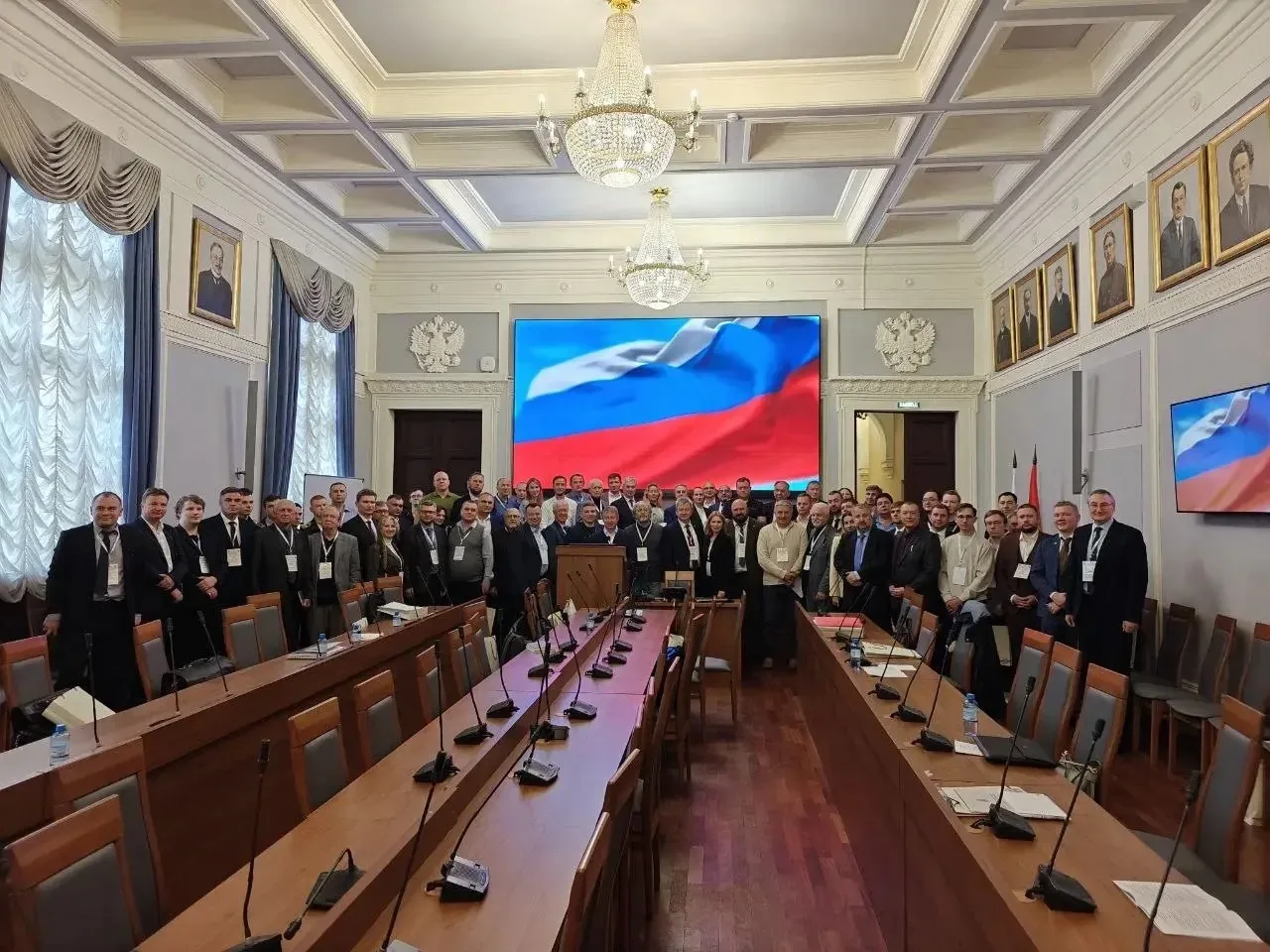 Групповое фото участников конференции на фоне экрана с изображением флага России.
