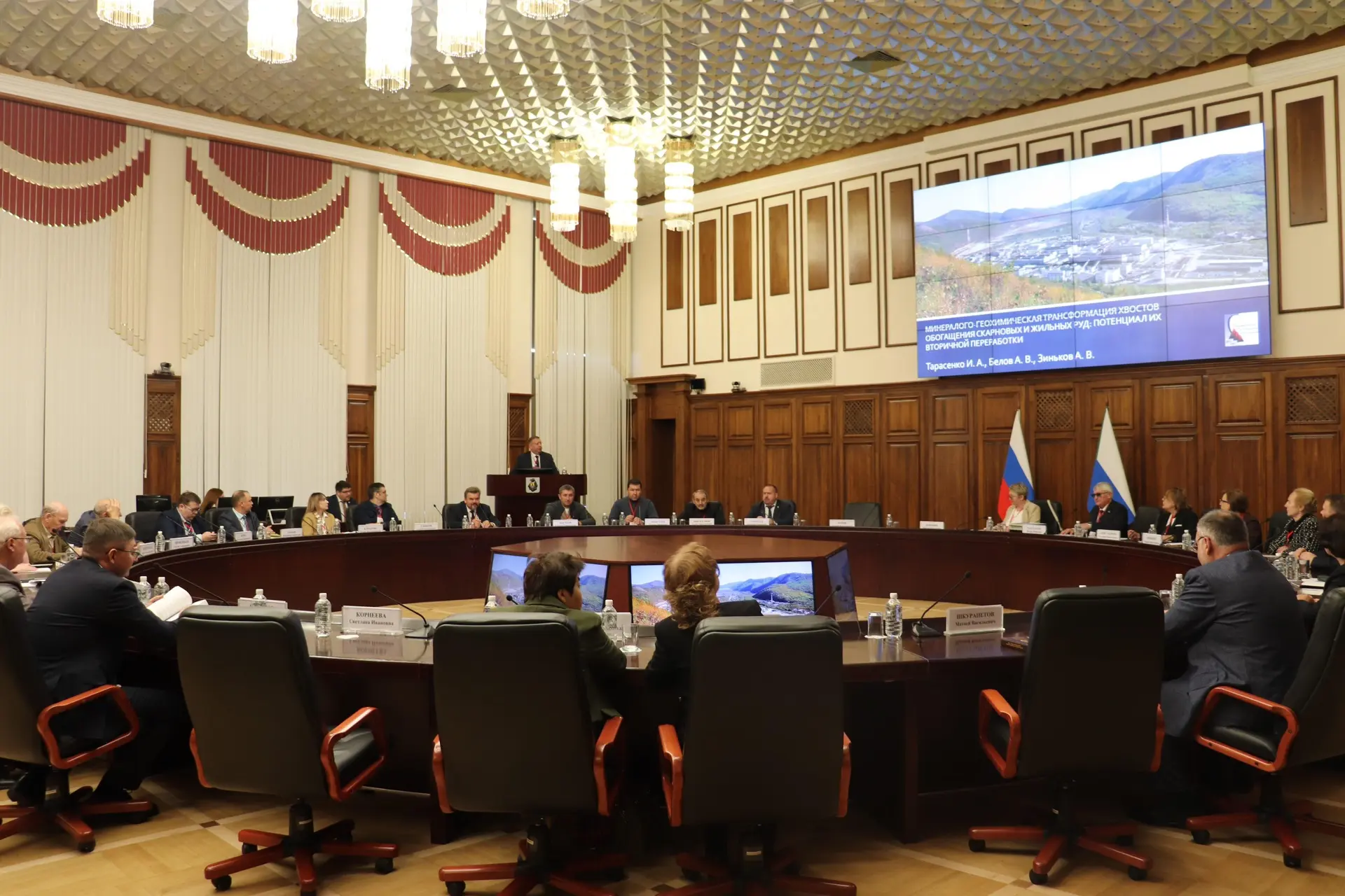 Meeting participants in the hall, with a presentation showing an image of a mining complex on the large screen.