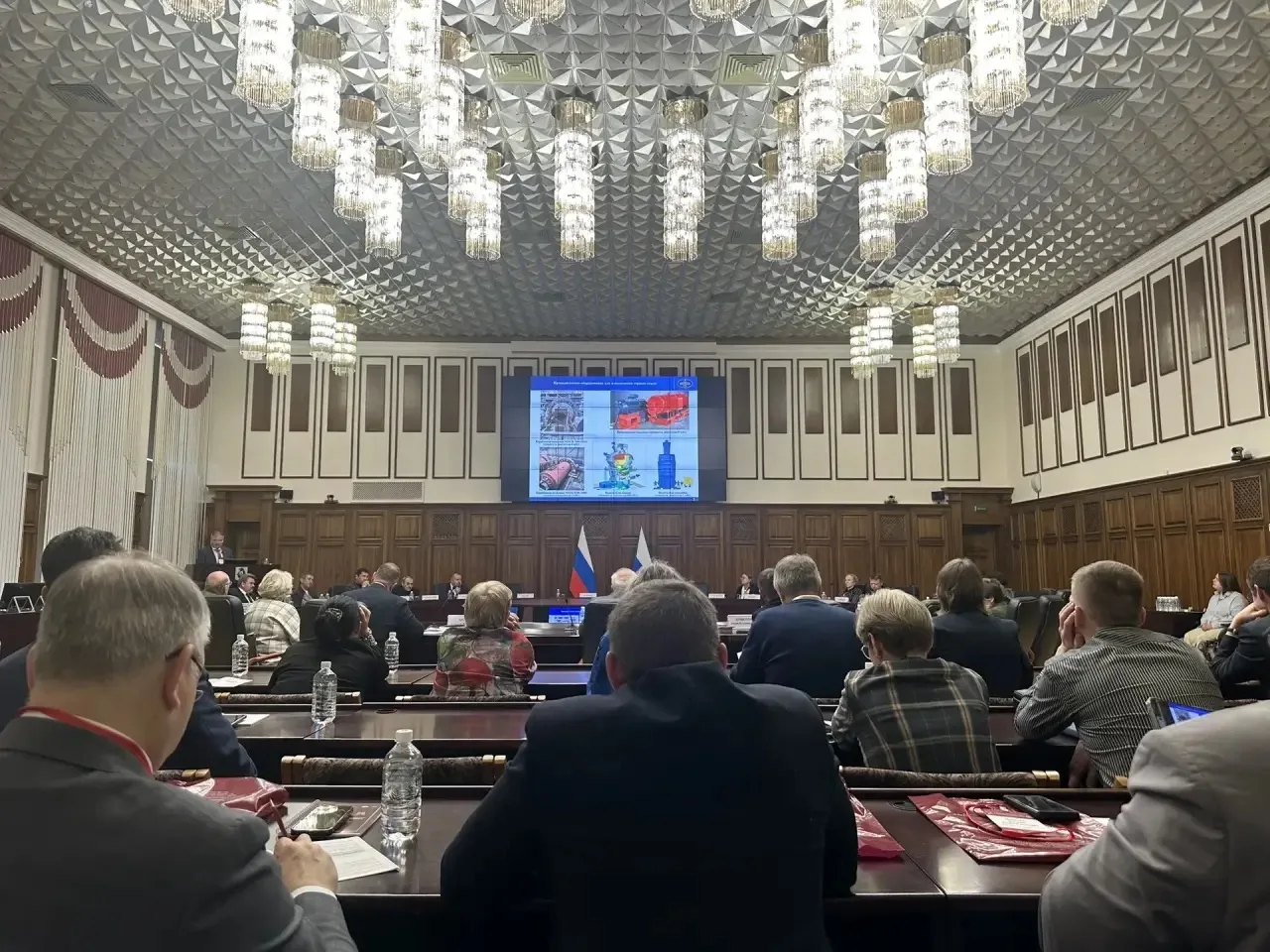 A meeting room, participants looking at a large screen displaying a complex diagram or graph.