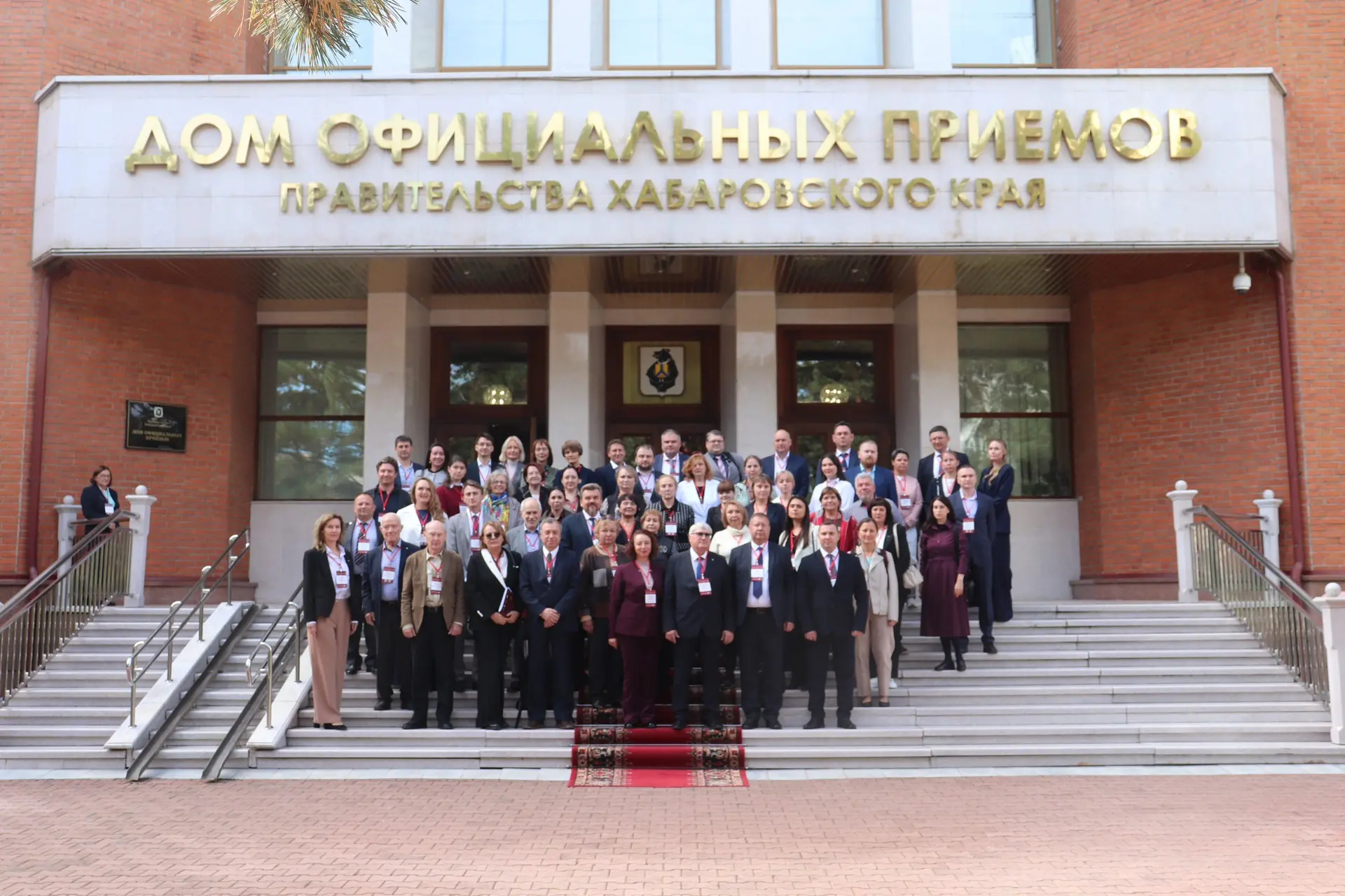 A group of people poses for a photo on the staircase in front of the 'House of Official Receptions of the Government of Khabarovsk Krai' building.