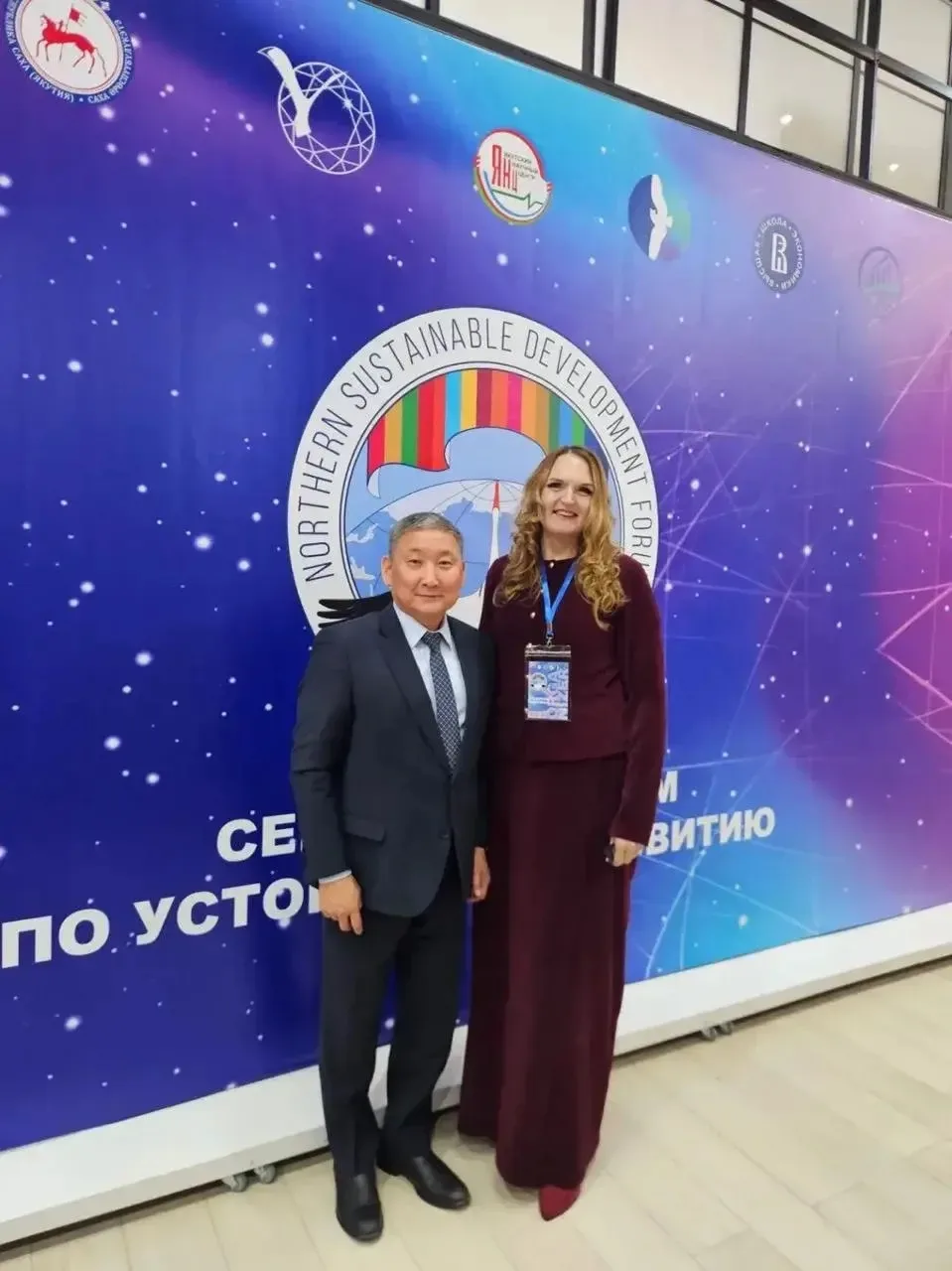 Надежда Филиппова и мужчина в костюме стоят на фоне баннера конференции "Northern Sustainable Development Forum".