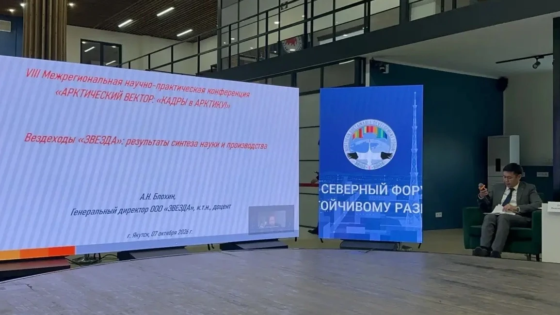 Экран с названием конференции «Арктический вектор» и темой доклада «Вездеходы ЗВЕЗДА: результаты синтеза науки и производства», человек в зале сидит на кресле.
