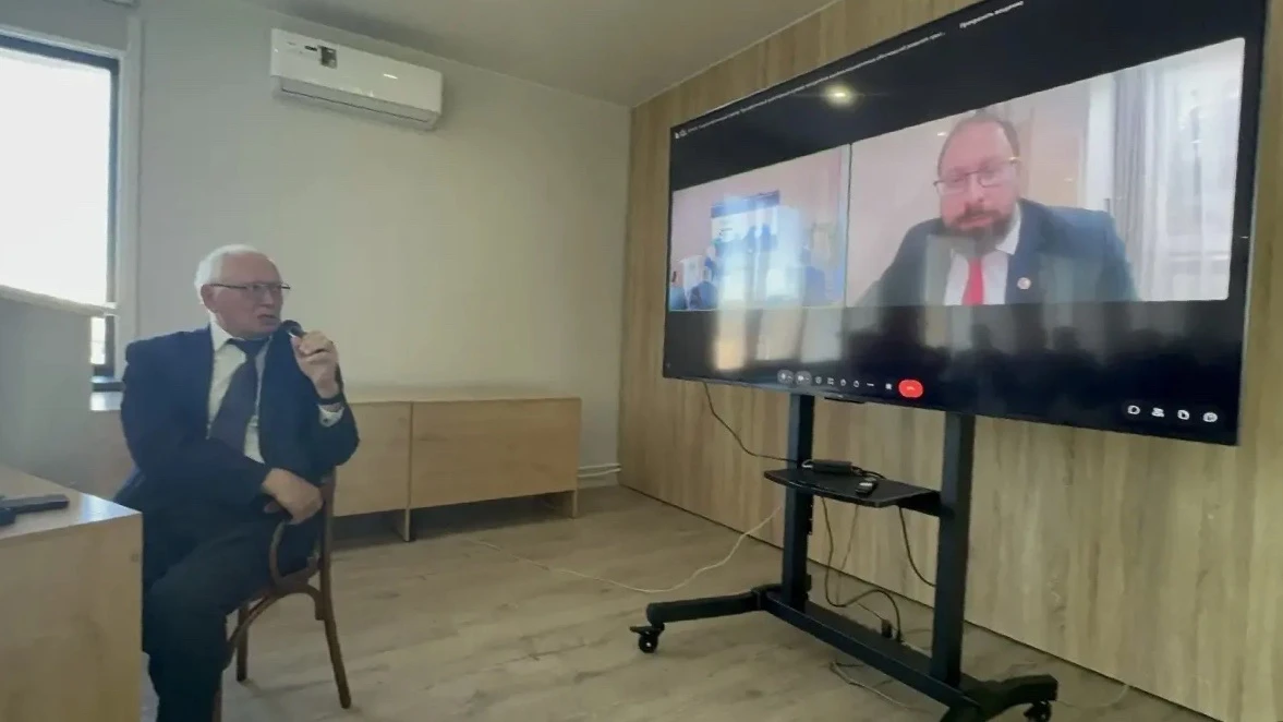 Участник семинара с микрофоном сидит напротив большого экрана, на котором видна онлайн-трансляция с Александром Блохиным.