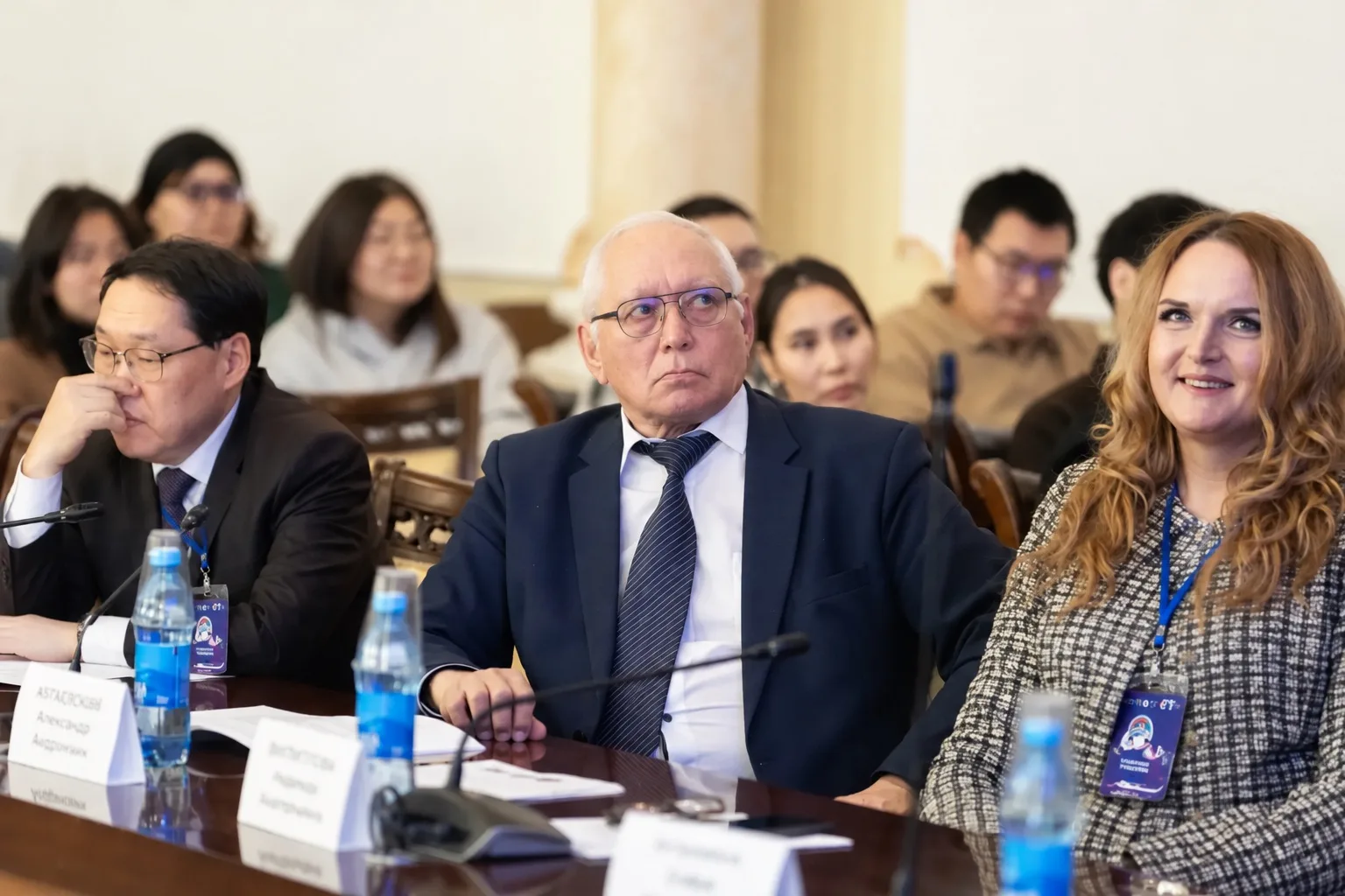 Группа участников конференции, мужчины и женщины, слушают доклад на заседании.
