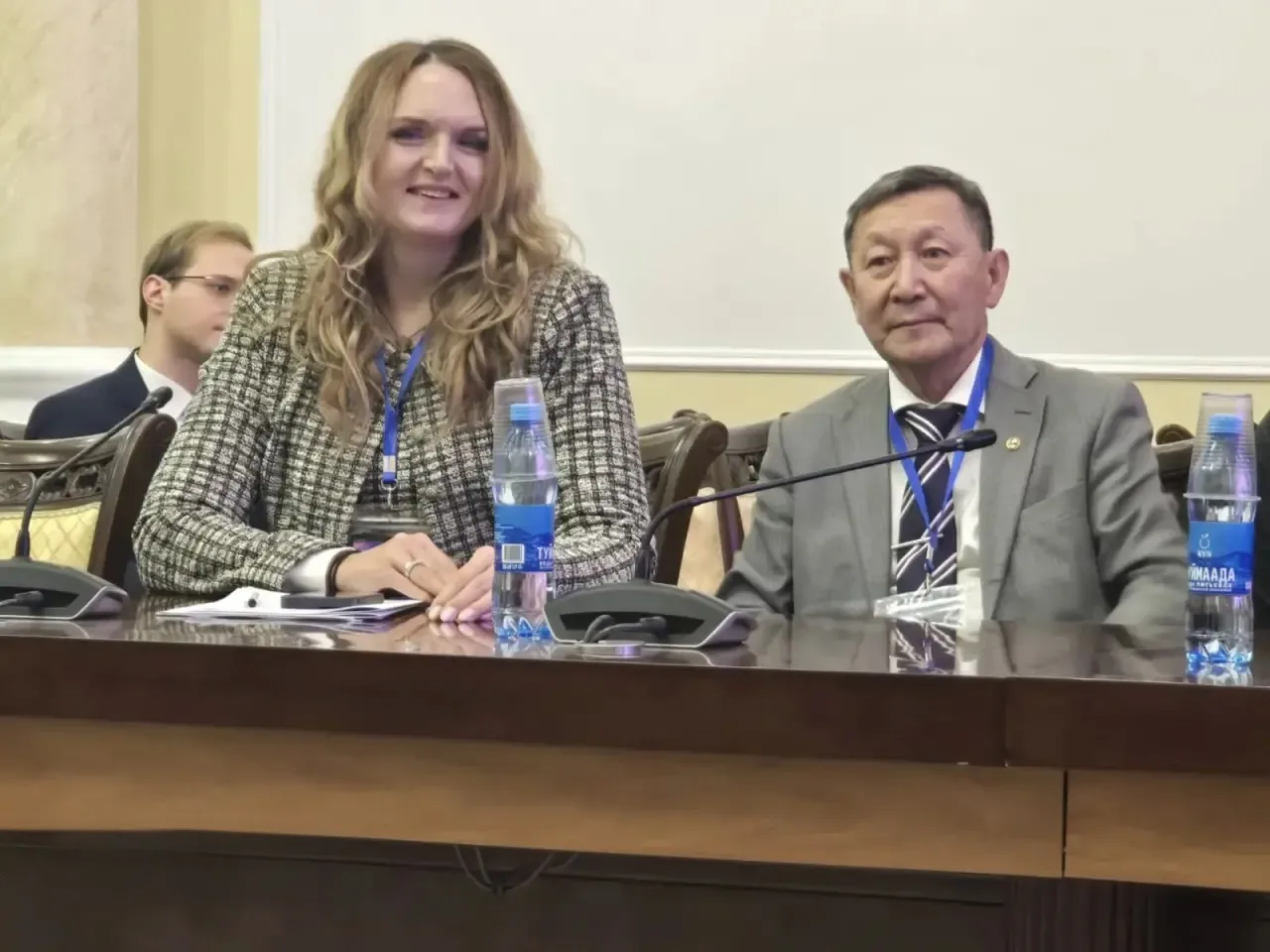 Крупный план женщины-докладчика и мужчины, сидящих за столом на конференции.