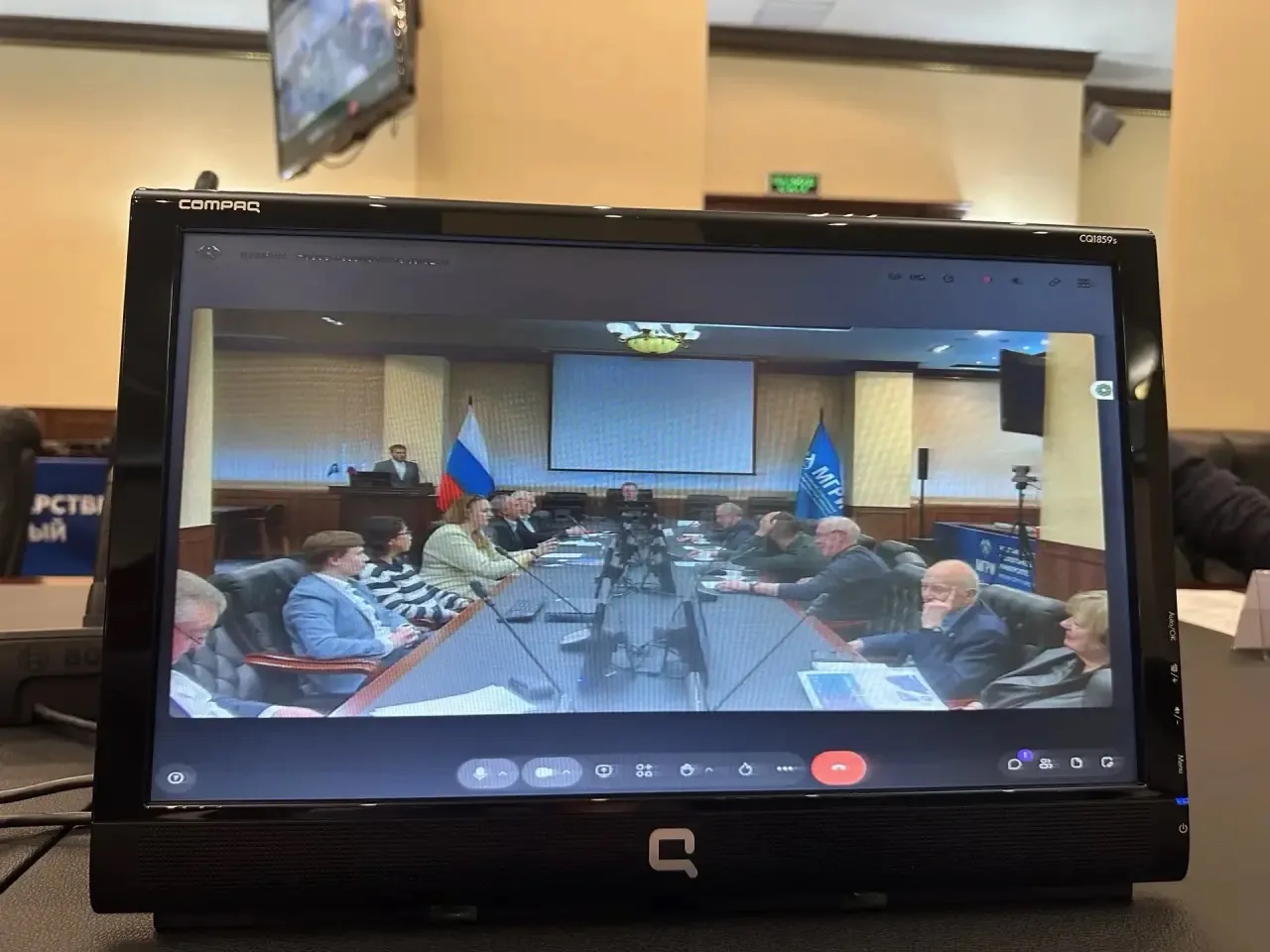 The monitor shows a video conference with round table participants.
